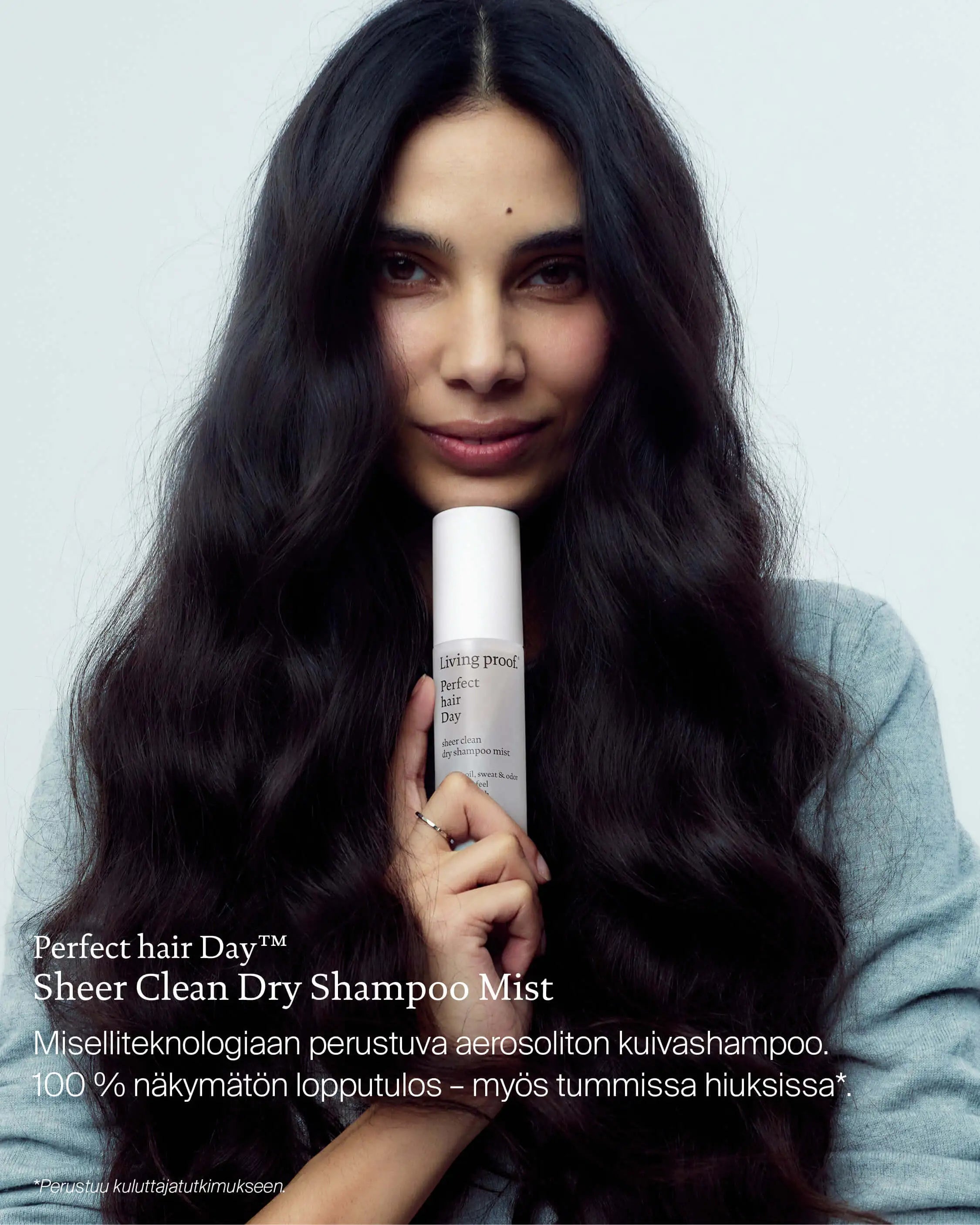 Nainen pitelee Living Proof Sheer Clean Dry Shampoo Mist -kuivashampoota tummien hiustensa edessä